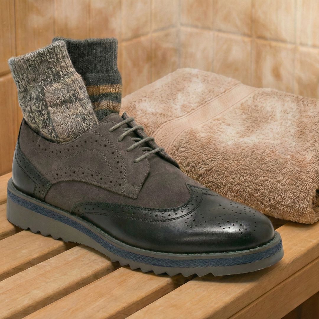 Gray brogue shoe with wool socks displayed on a wooden bench near a folded towel.